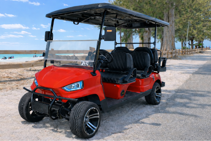 Red golf cart parked on a beachside road with trees and ocean view.