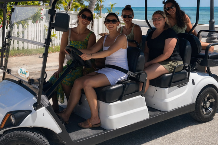 Five people smiling on a golf cart near the beach.
