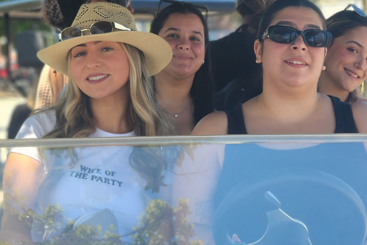 Four women smiling and sitting in a golf cart outdoors.