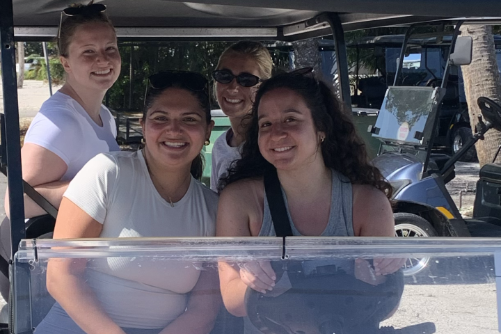 Four people smiling while sitting in a parked golf cart.
