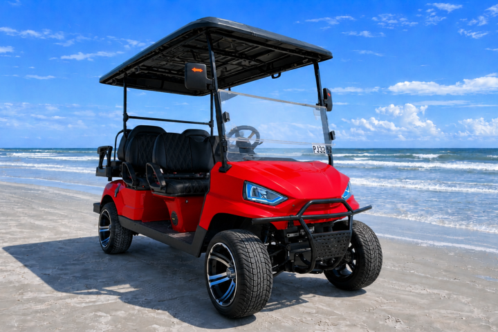 Red golf cart parked on a sandy beach with ocean and blue sky in the background.