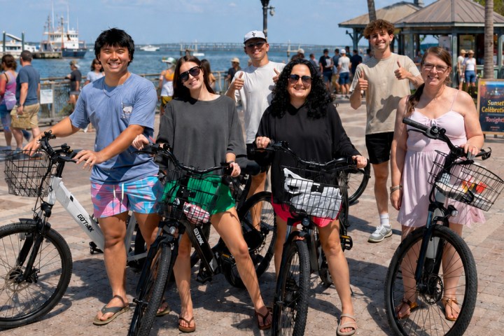 Group of people with bicycles posing near the ocean on a sunny day.