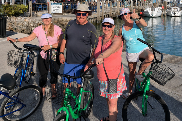 Four people with bicycles near a waterfront, smiling and posing for a photo.