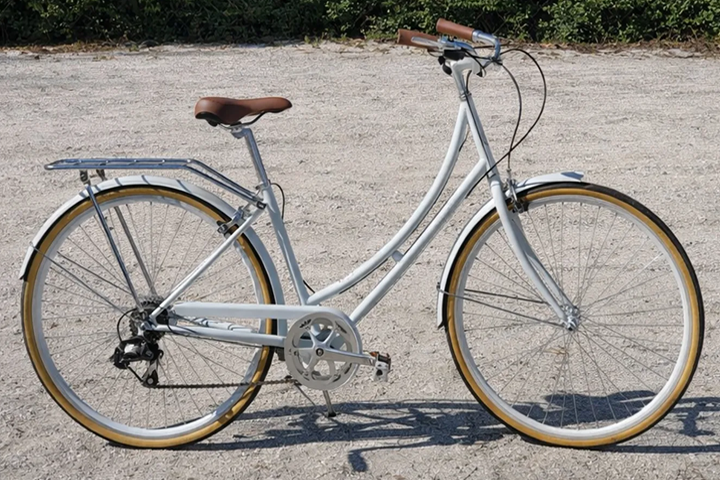 White city bicycle with brown seat and handles on a gravel surface.