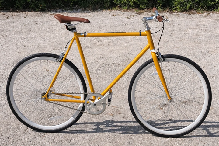 Yellow bicycle with brown seat on a gravel path.